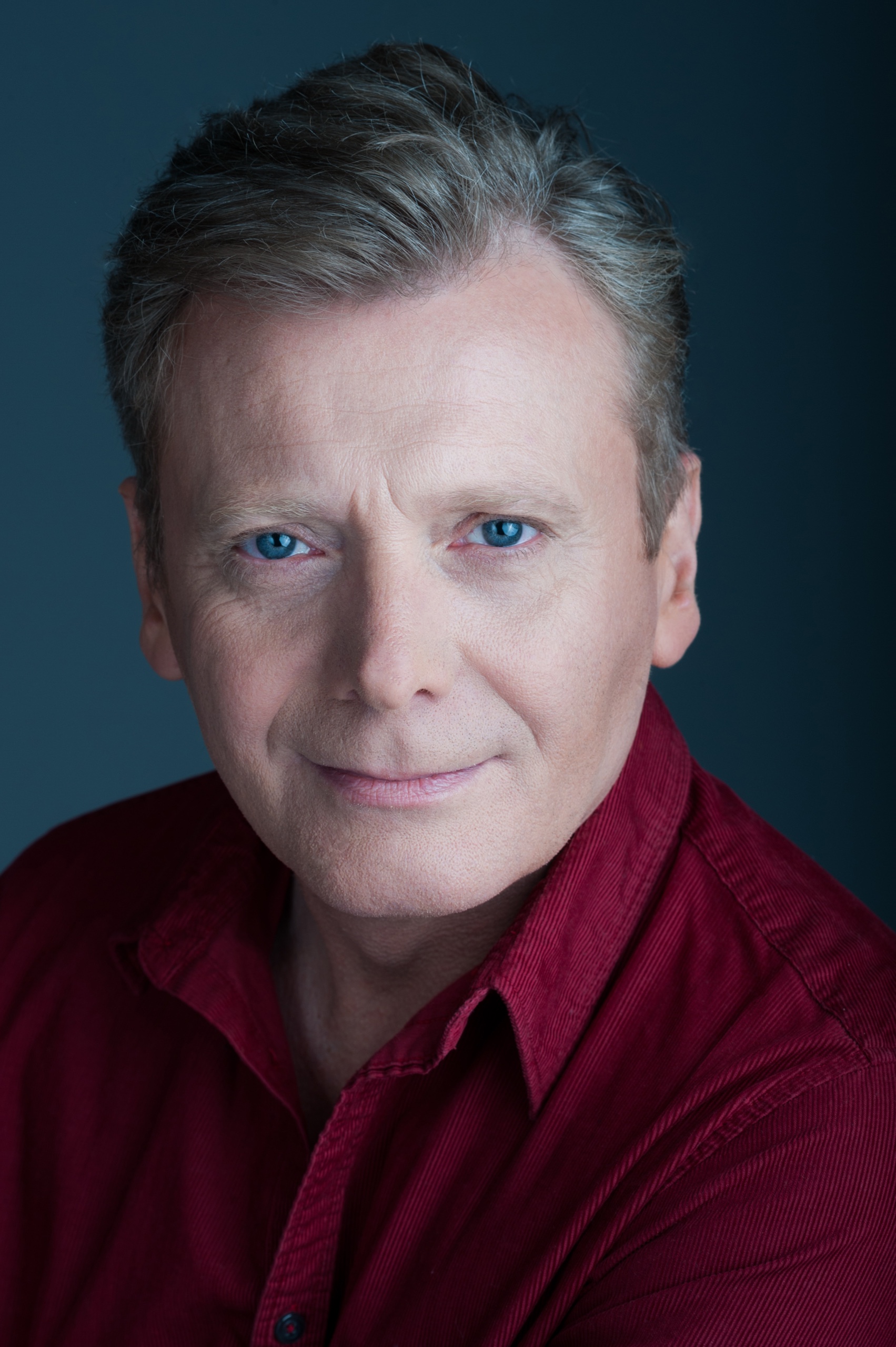 Uśmiechnięty mężczyzna w bordowej koszuli na granatowym tle, portret w studio